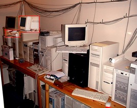 Kvalito serverpark, en utrolig mengde mikrodatamaskiner av alle slag bortetter, både over og under to lange kontorbord, med ethernetkabler hengende på veggen og i taket.